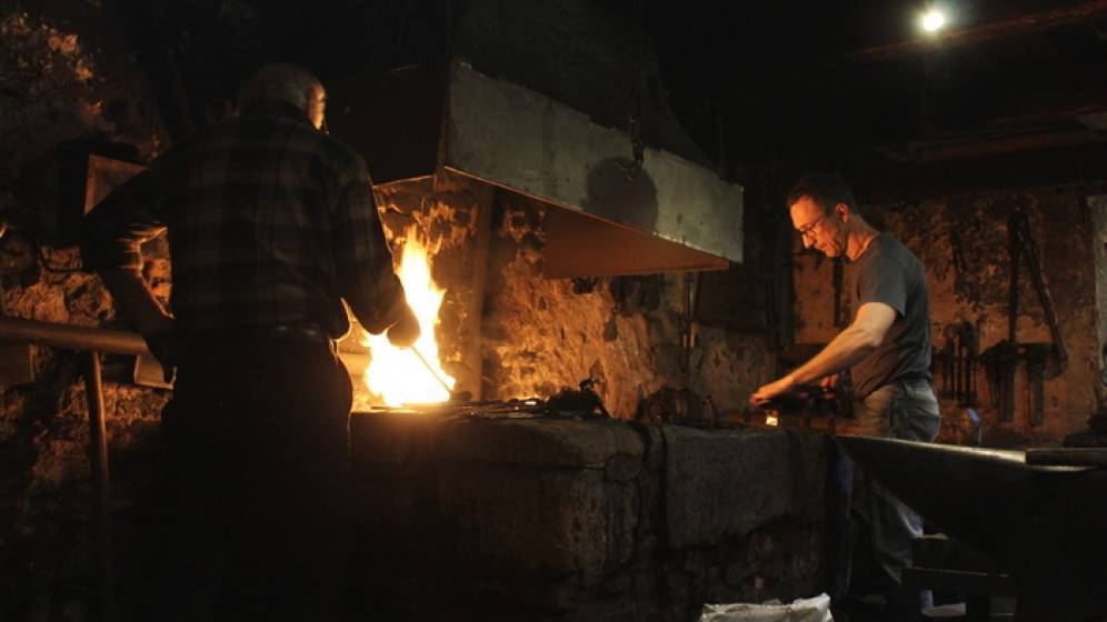 Photographie de la forge d'Étueffont (90), deux forgerons se tiennent devant la forge