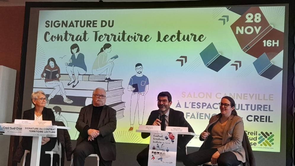 Photo de l'événement de signature du Contrat Territoire Lecture, organisé le 28 novembre 2024 dans le Salon Canneville de l’espace culturel La Faïencerie à Creil. Sur scène, quatre intervenants assis participent à la cérémonie. Derrière eux, un écran affiche le titre de l'événement : 'Signature du Contrat Territoire Lecture', accompagné de visuels illustrés de personnages lisant des livres et des détails informatifs, tels que la date et le lieu. L'atmosphère est professionnelle et conviviale, avec des participants attentifs en premier plan.