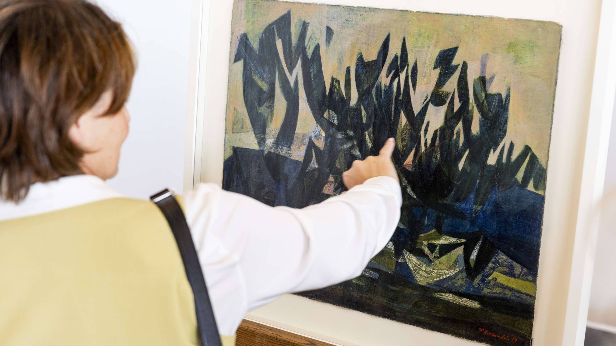 photo d'une femme de dos en train de regarder et de montrer un tableau