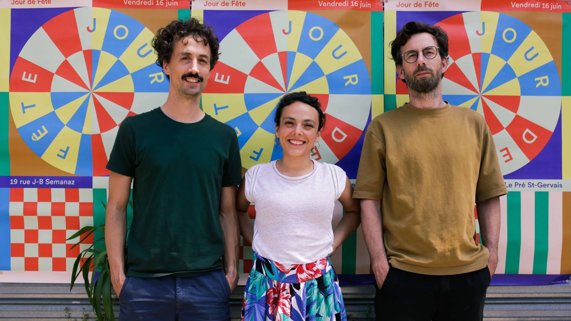 photo de trois personnes, une femme entourée de deux hommes souriants sur un fond coloré