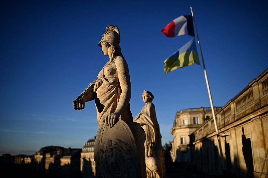 photo prise depuis le toit d'un opéra avec deux statues au premier plan, les drapeaux ukrainiens et français au second plan sous un ciel bleu