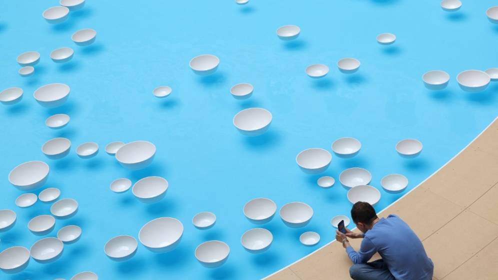 photo prise d'en haut d'un bassin avec des gouttes blanches flottant à la surface. Au bord du bassin, un homme assis prend une photo