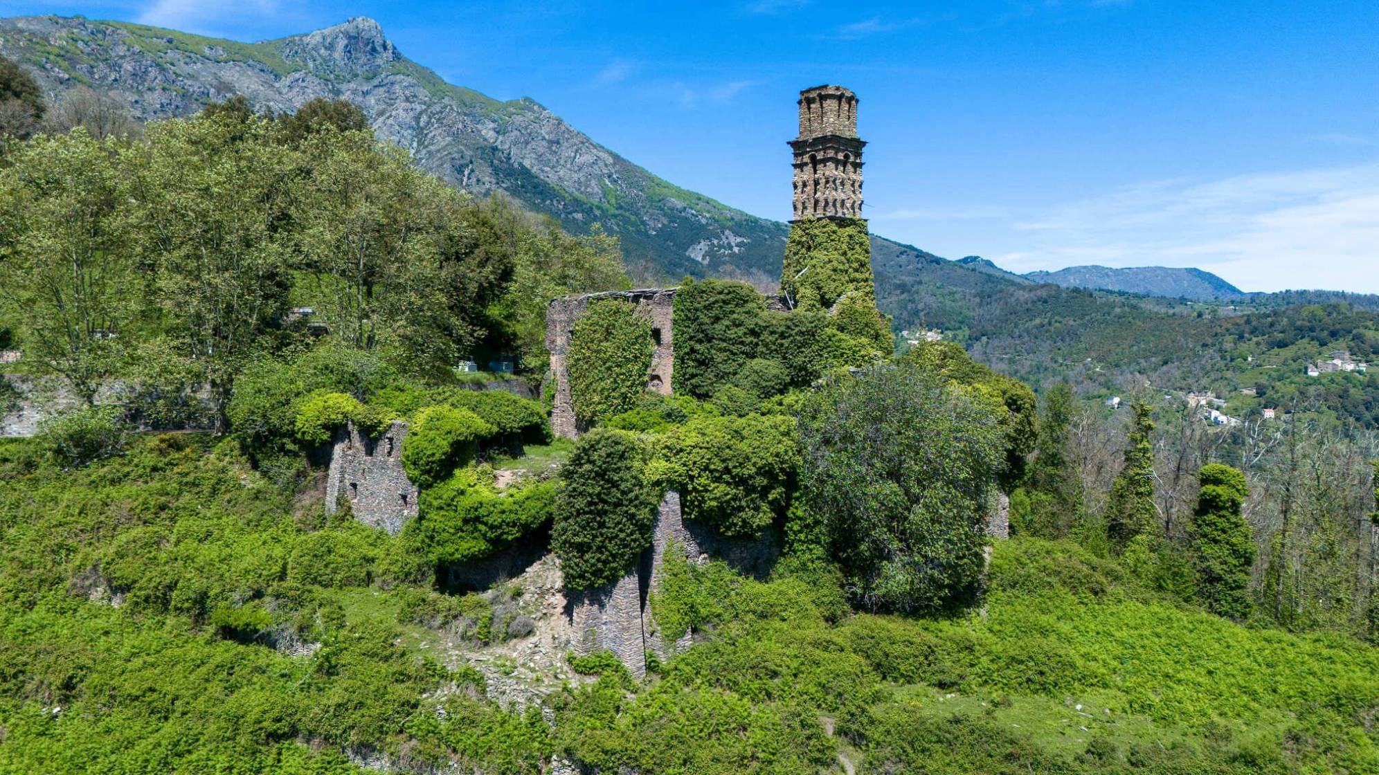photo d'un couvent dans un paysage de montagne. le couvent est en ruine, recouvert par des arbres et de la végétation