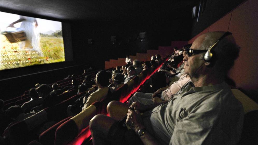 photo d'une salle de cinéma avec une personne au premier plan déficiente visuel assise qui a un casque sur les oreilles pour suivre le film