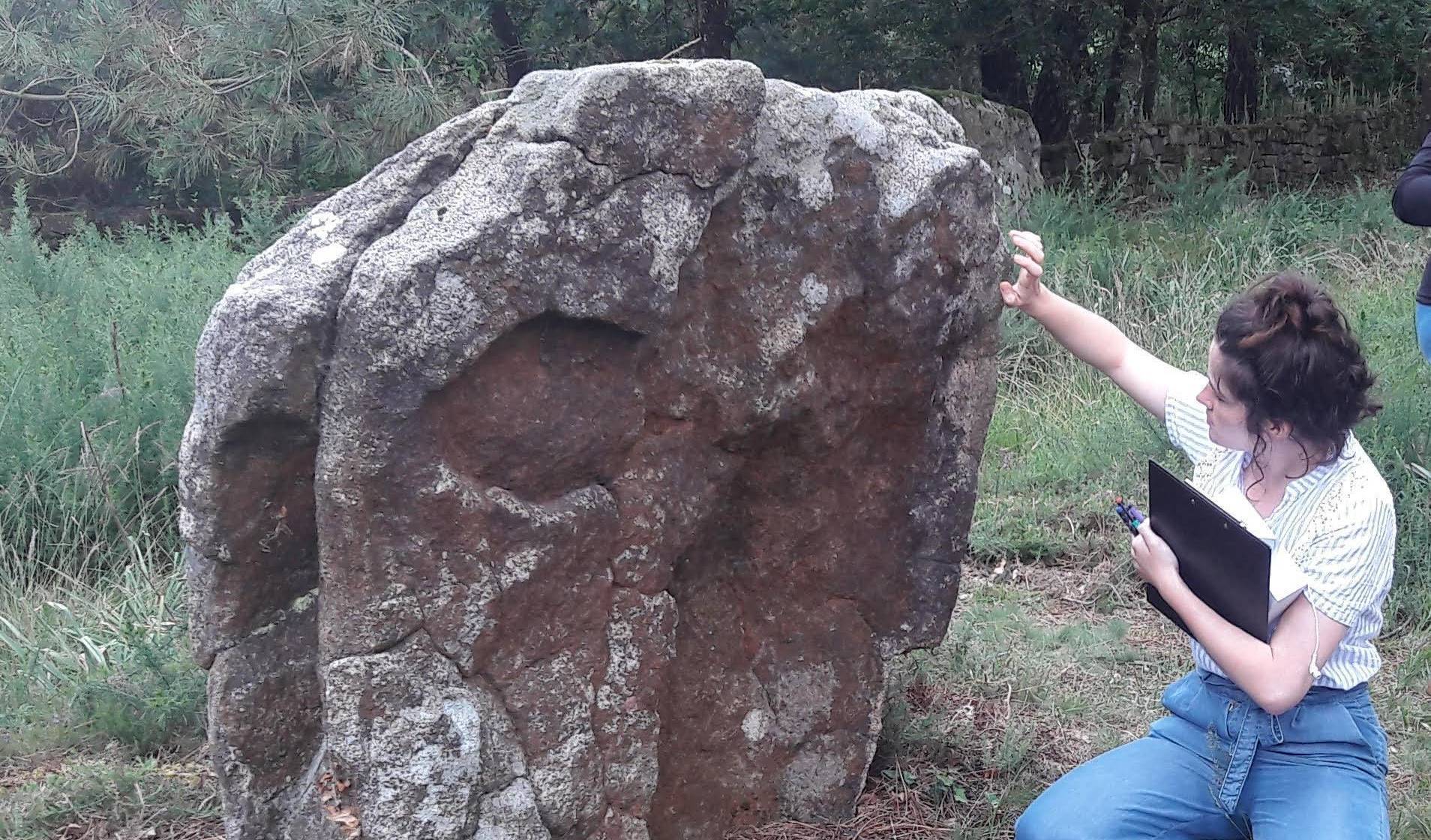 Une jeune femme observe un menhir en vue d'établir un constat d'état.