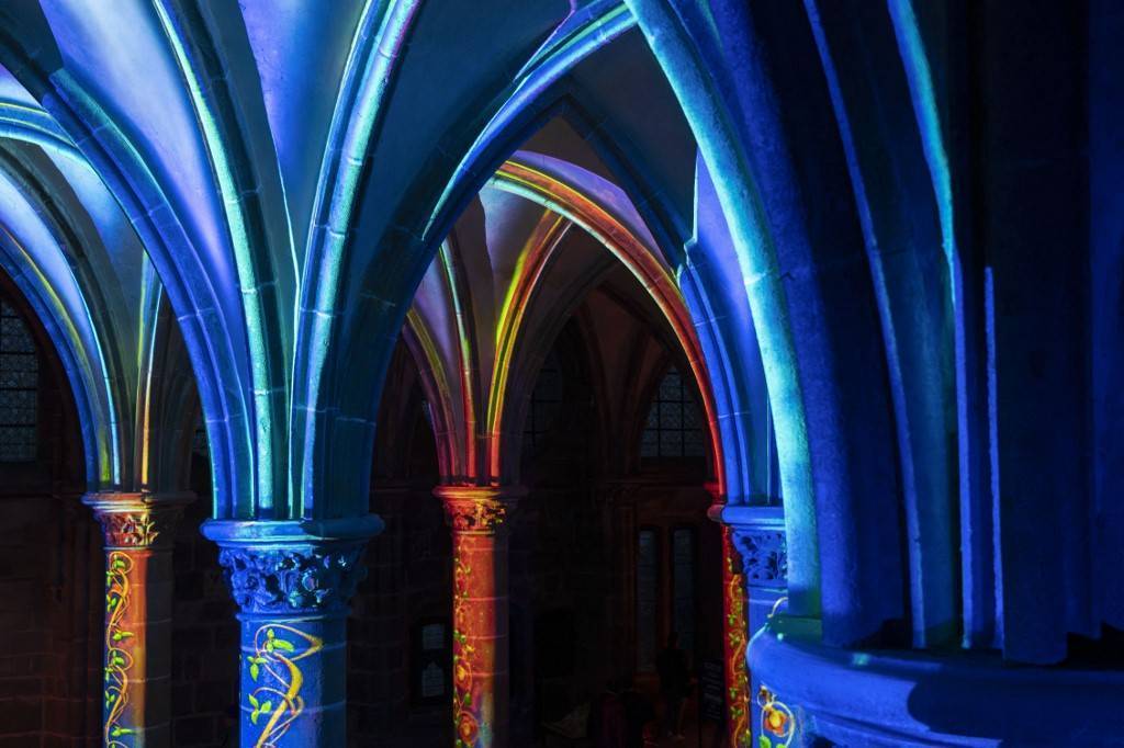Les colonnes de l'Abbaye du Mont Saint-Michel sont éclairées par des lumières aux reflets bleu-orangé.