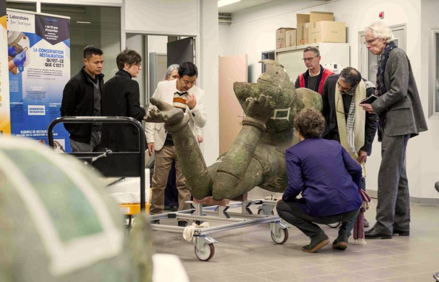 Examen par un groupe de personnes de la statue colossale en bronze du Vishnou couché du Mébon occidental, au laboratoire Arc'Antique