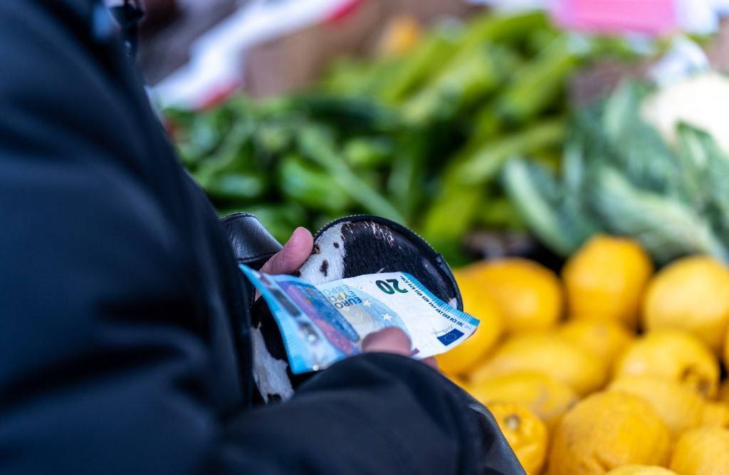 photo d'une personne tenant son porte monnaie avec des billets devant un stand de fruits et légumes