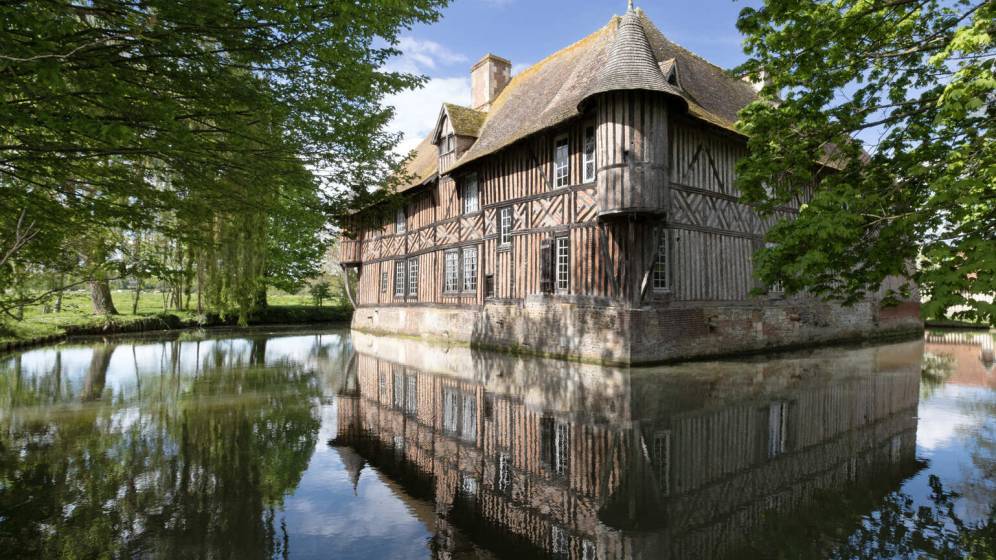 Photo du manoir de Coupesarte en Normandie, maison à colombage au bord d'un plan d'eau avec des arbres